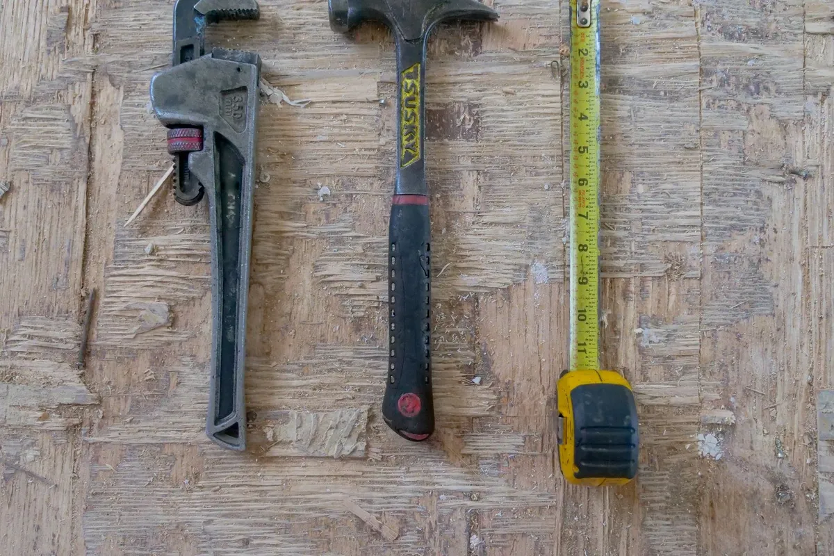 Close-up of a hammer, wrench, and measuring tape on a wooden surface, tools used in boiler installations.