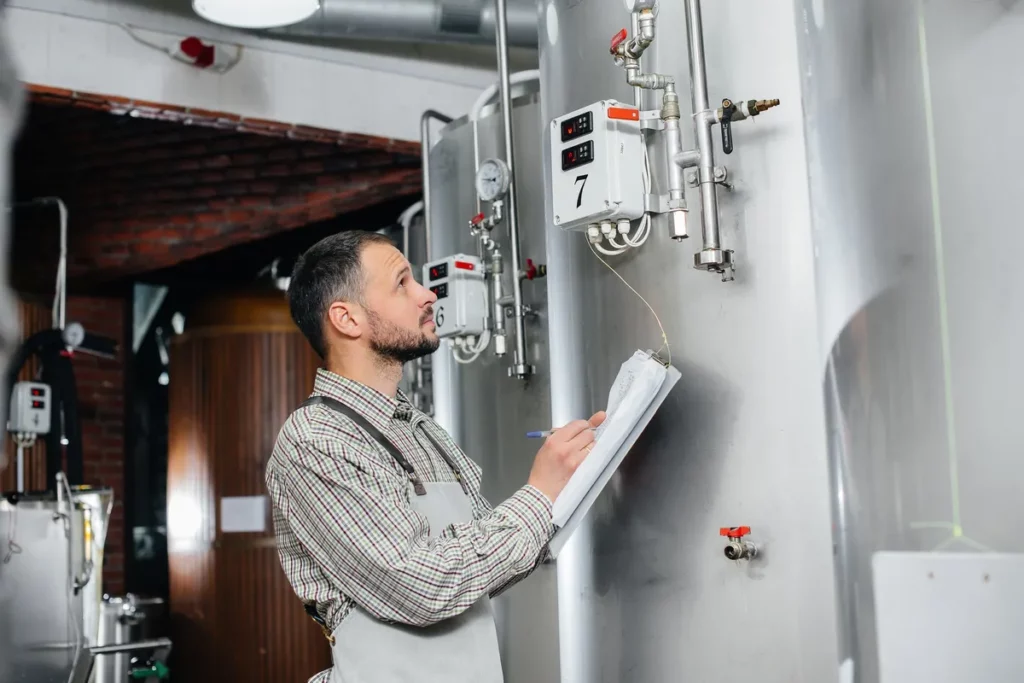 A young bearded brewer checks sensor readings while brewing beer, highlighting precision in installations.