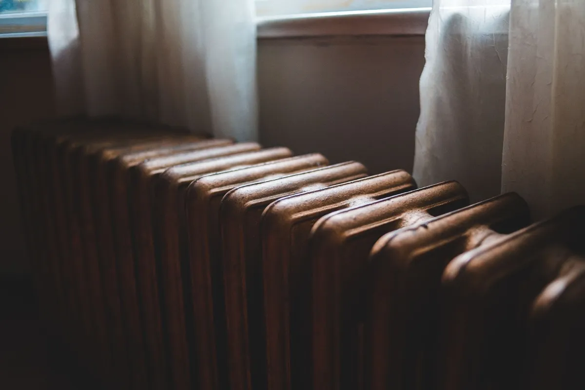Old cast iron heating battery by a windowsill with curtains, highlighting considerations for boiler installations.