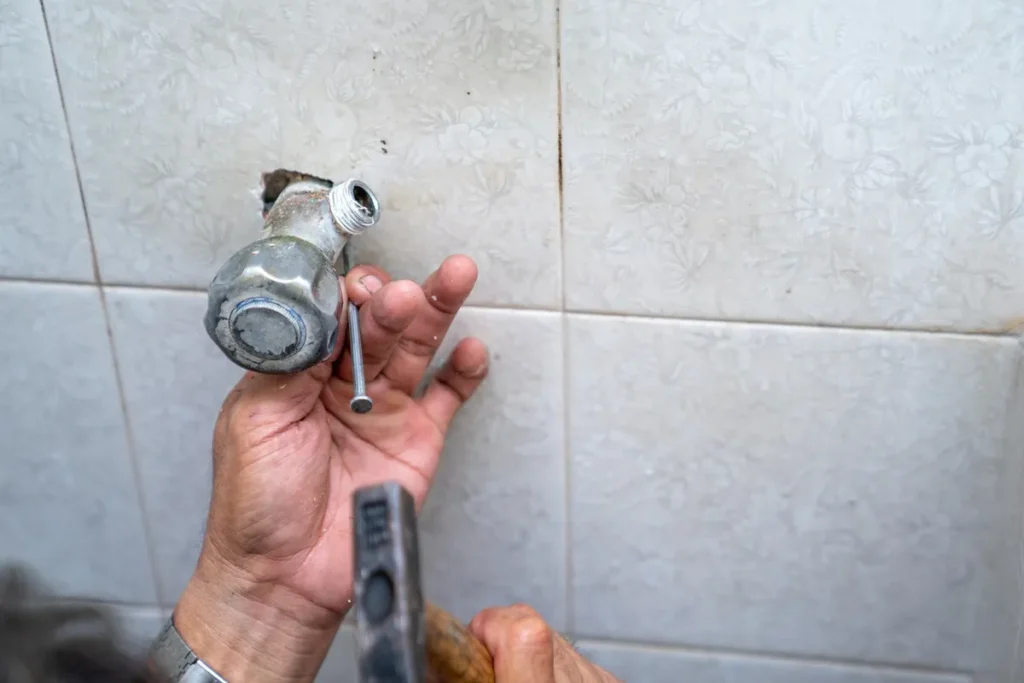 An Asian man attempts to repair a leaking shower pipe in an old restroom, highlighting the need for emergency plumbing.