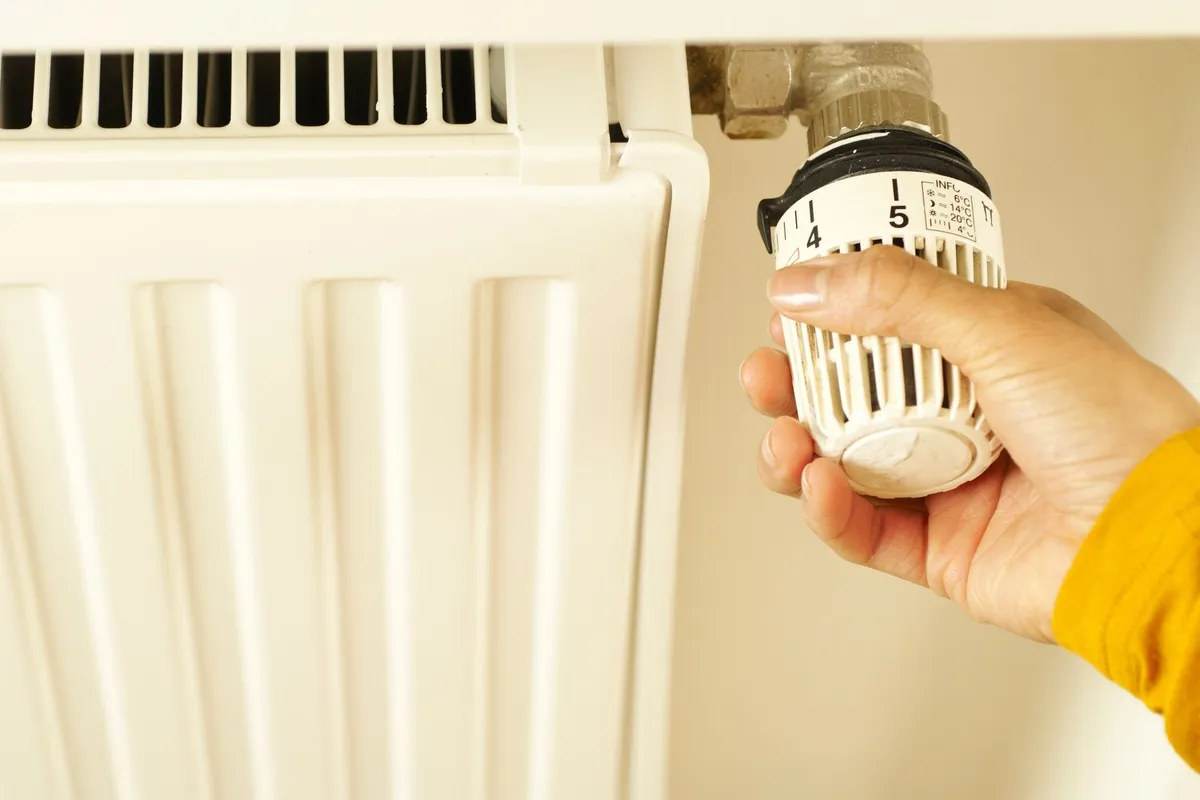 A hand adjusting a radiator thermostat to manage home heating temperature for safety and efficiency.